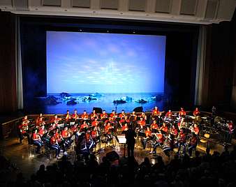 Orchester und Tanzgruppe in blauem Licht auf der Bühne