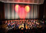 Orchester beim Konzert Kids winds, Bühnenvorhang mit rotem Licht angestrahlt